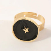 Gold-toned adjustable ring with a black, textured circular face featuring a small gold star in the center.