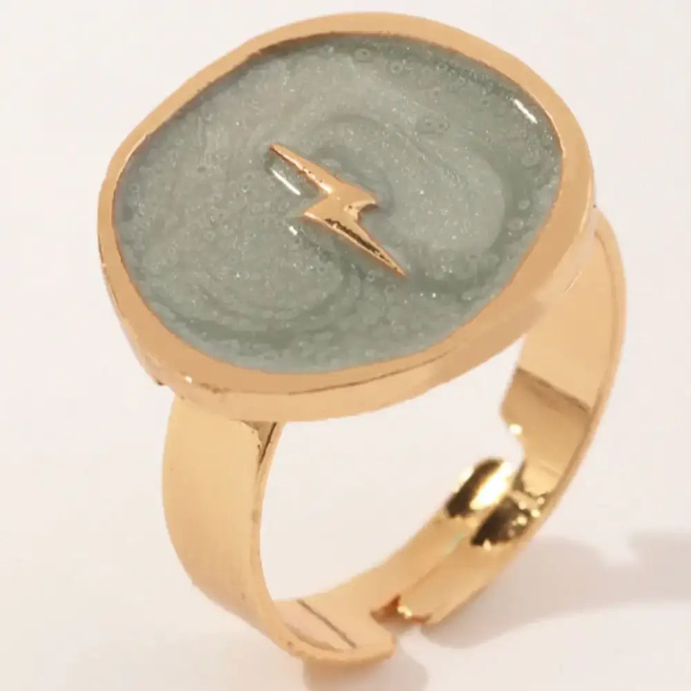 Gold-toned ring with a circular, translucent green resin face featuring a small gold lightning bolt emblem.