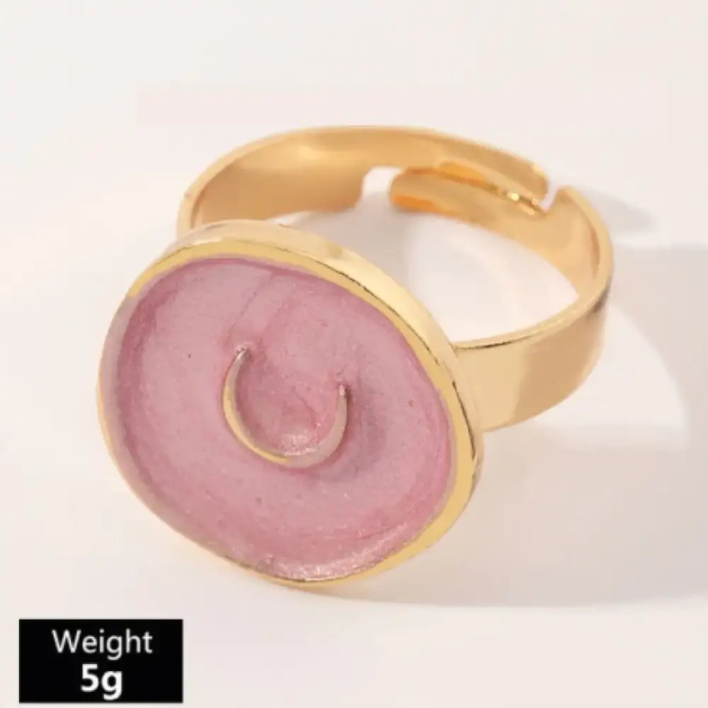 A pink enamel smiley face ring with a gold-toned metal band and adjustable sizing.