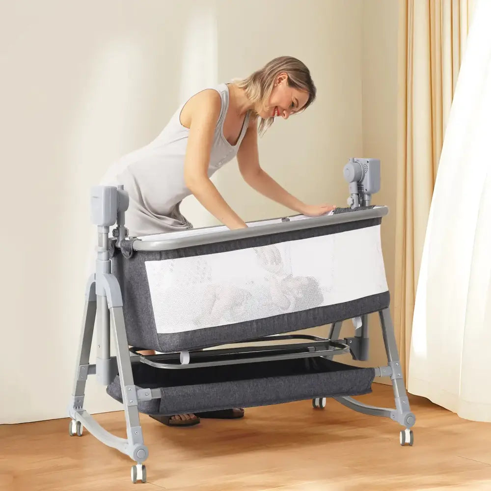Gray and white convertible baby bassinet with mesh sides, adjustable height, wheels for mobility.