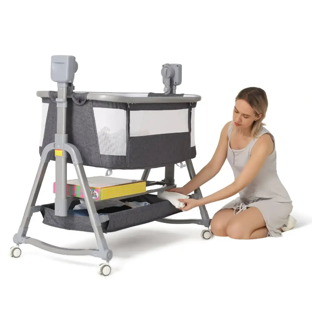 Gray and white baby cradle with adjustable height, mesh sides for visibility, and wheels for mobility.