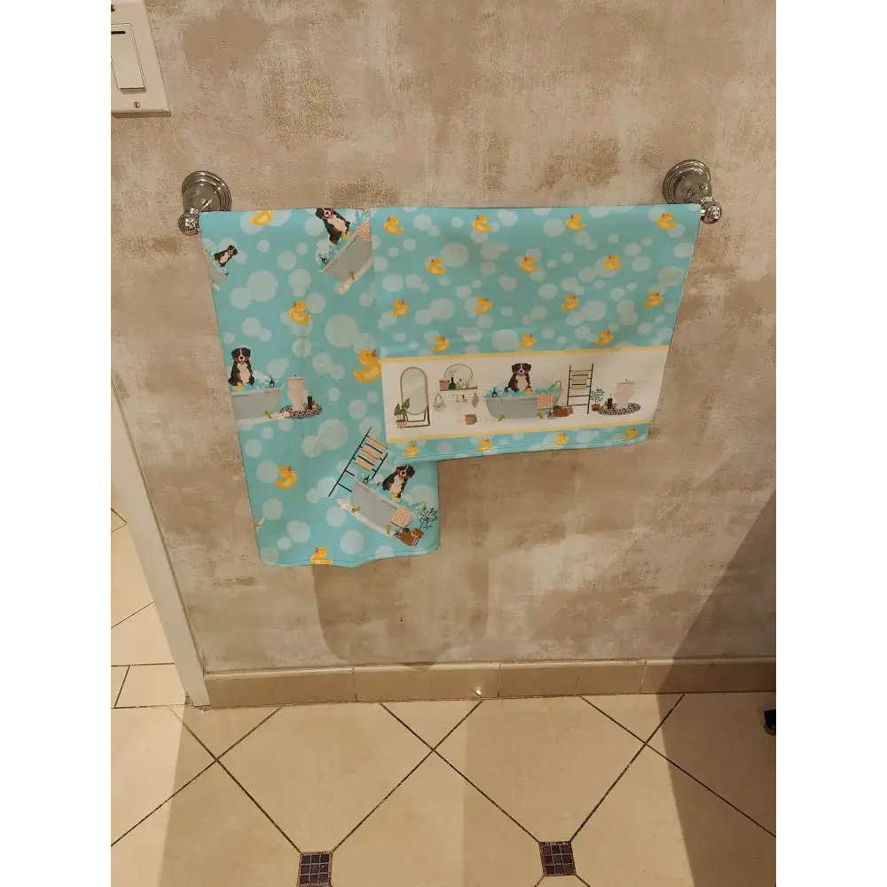 Light blue towel with a playful pattern of yellow rubber ducks and black-and-white dogs in bath scenes, hanging on a silver rack.