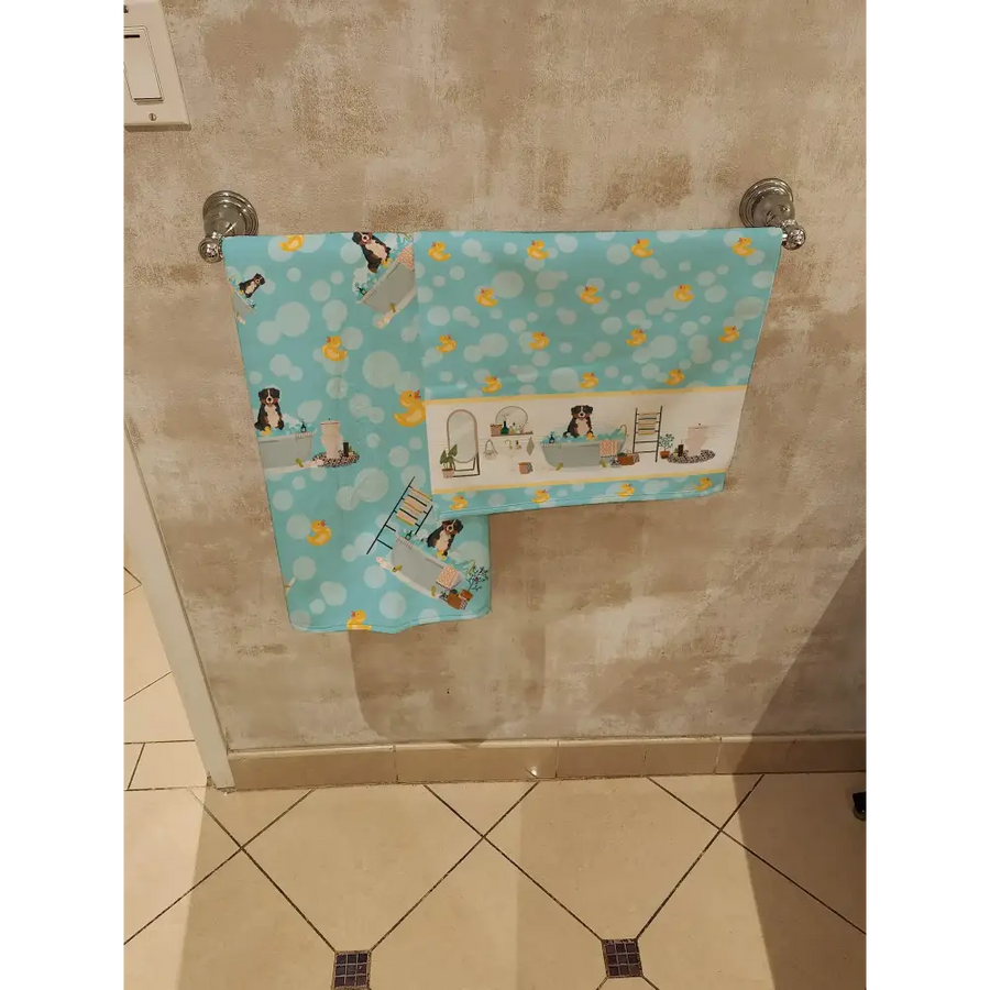 Light blue towel with a playful pattern of yellow rubber ducks and black-and-white dogs in bath scenes, hanging on a silver rack.