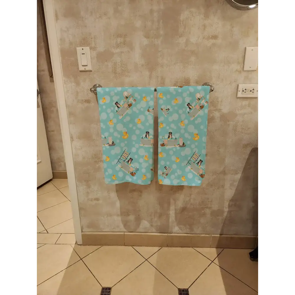 Two light blue towels with a playful pattern of penguins and yellow rubber ducks hanging side by side on a metallic towel rack.