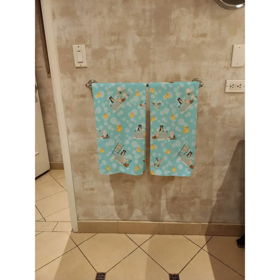 Two light blue towels with a playful pattern of penguins and yellow rubber ducks hanging side by side on a metallic towel rack.