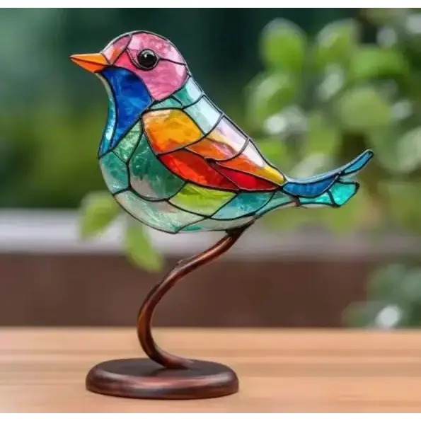 A vibrant, multicolored stained glass bird figurine with a pink head, orange beak, and rainbow-patterned body mounted on a curved bronze stand.