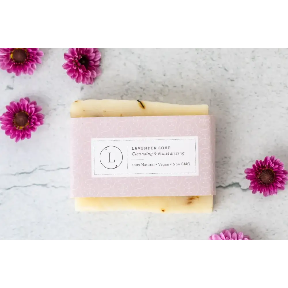 A pale lavender-wrapped bar of soap with a creamy off-white body and dark speckles, labeled ’lavender soap’ in elegant typography.