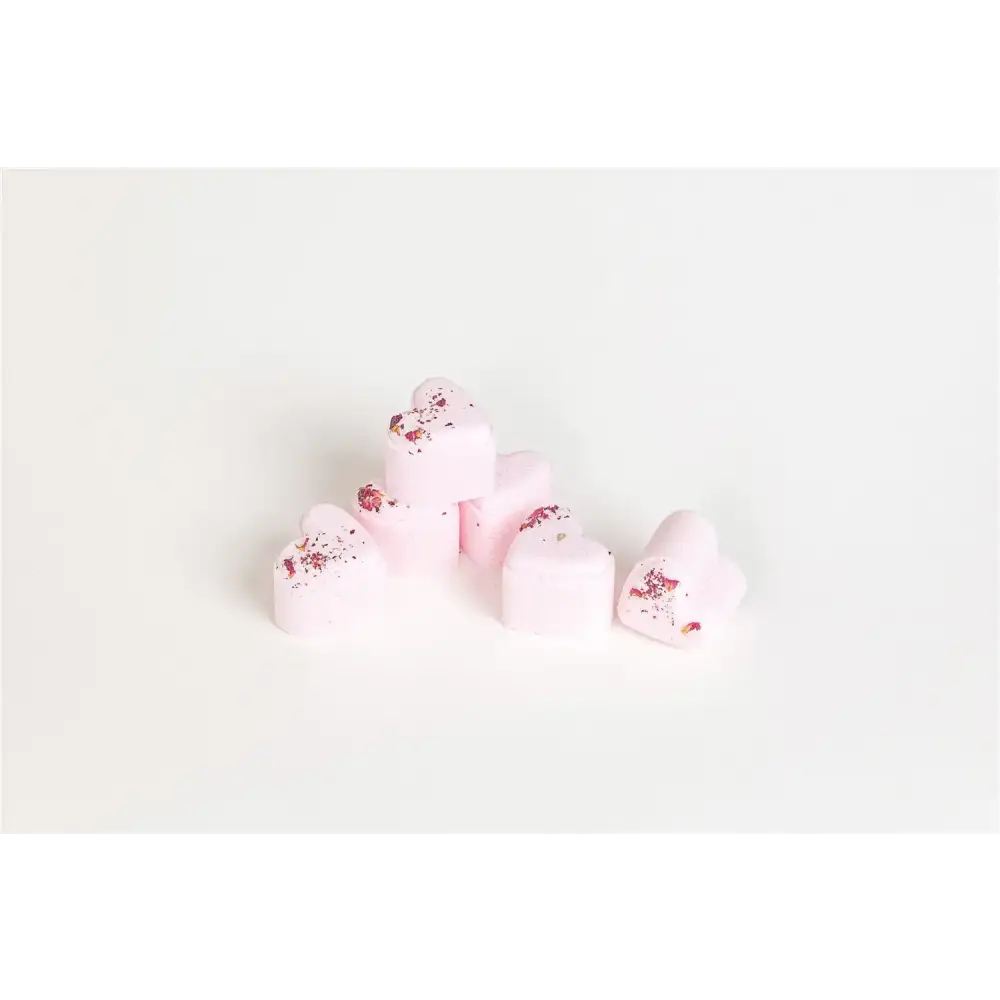 Pink heart-shaped bath bombs with dried rose petals scattered on top.
