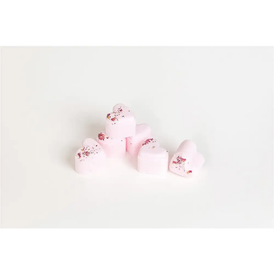 Pink heart-shaped bath bombs with dried rose petals scattered on top.
