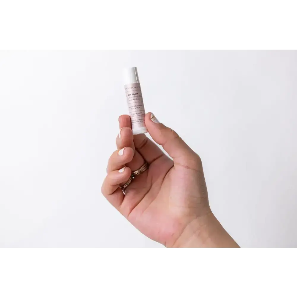 A sleek, white cylindrical tube of lip balm with a minimalist label and silver cap.