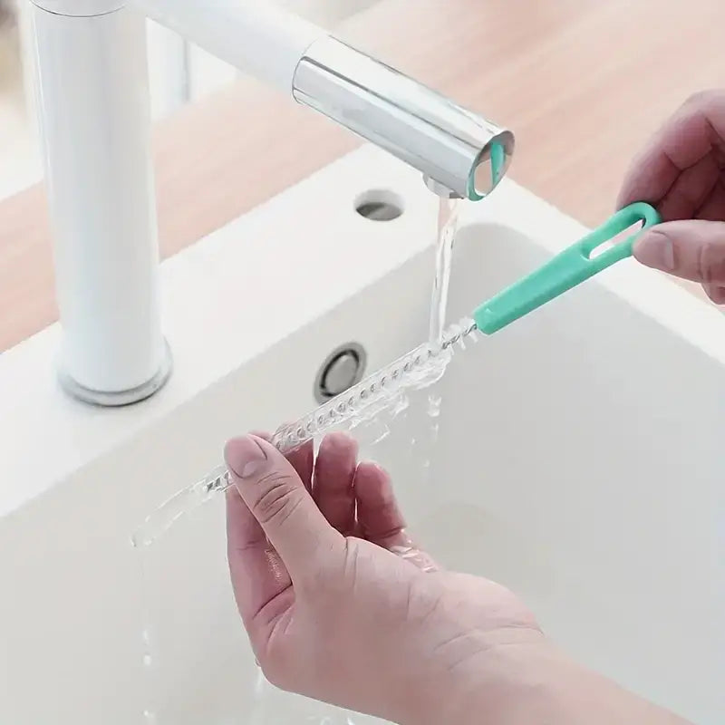 A clear, spiral-shaped bottle brush with a mint green handle is being rinsed under running water.