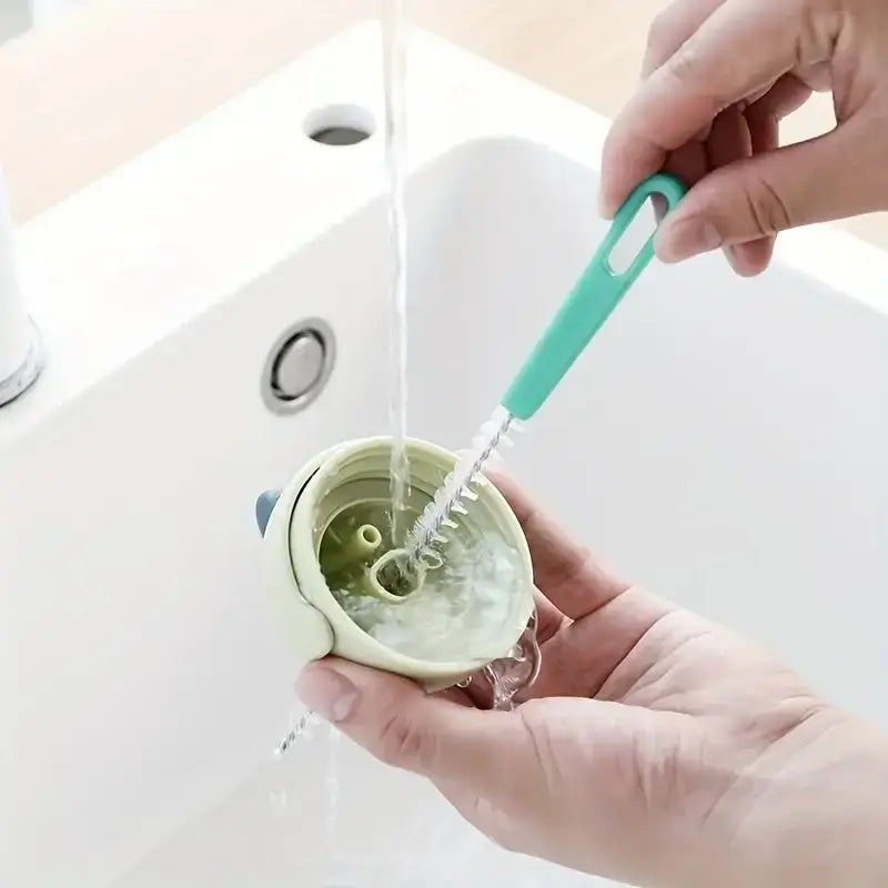 A mint green silicone bottle brush with a flexible, spiral bristle head is being used to clean the inside of a light green baby bottle.