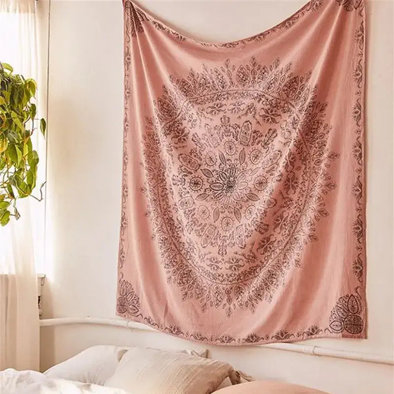A soft pink, velvet-textured tapestry with intricate dark brown mandala patterns hangs on a wall.
