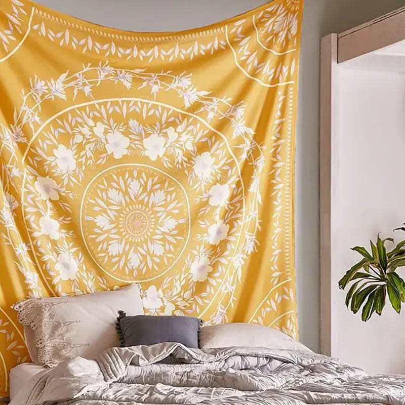 A vibrant yellow mandala tapestry with intricate white floral and leaf patterns, hanging as a decorative wall piece above a bed.
