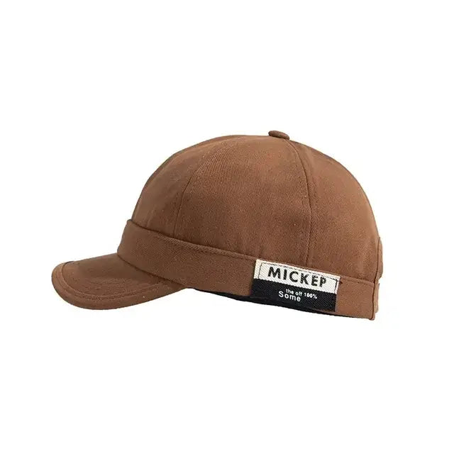 Brown cotton baseball cap with a black and white label on the brim reading ’mickep’ and ’the of 100% some.’