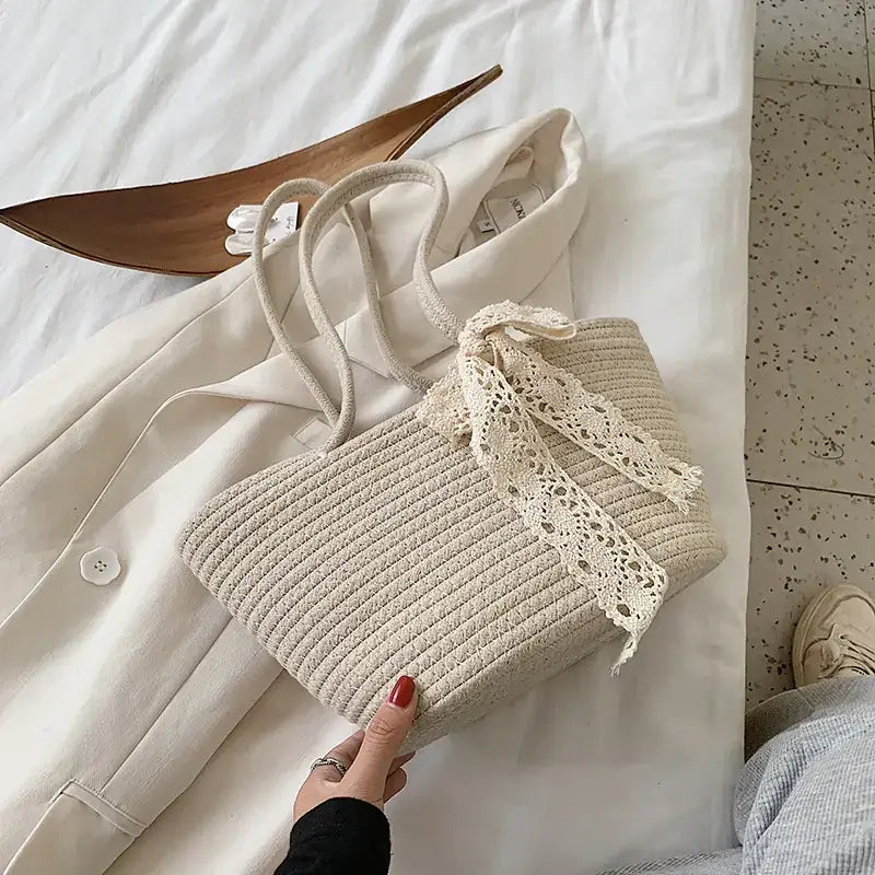 Beige woven straw tote bag with delicate cream lace bow and matching handles.