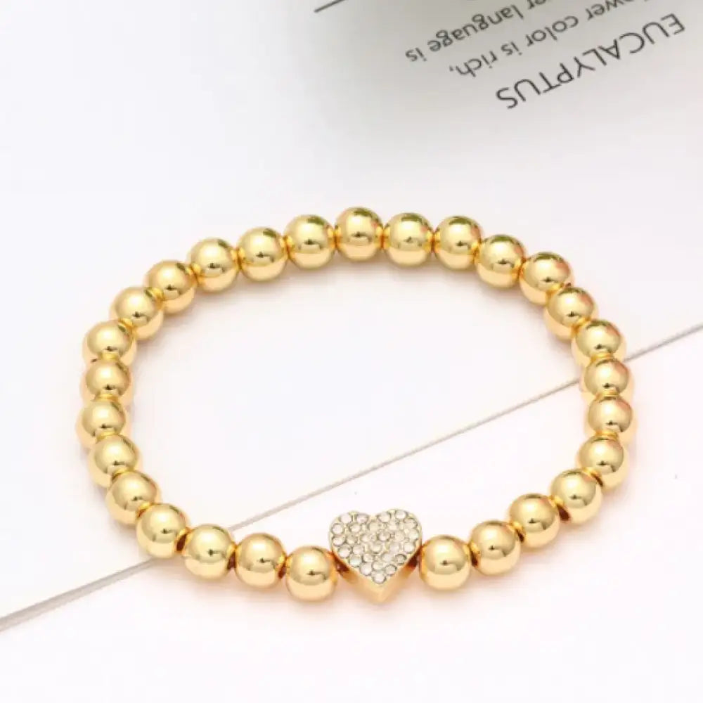 Gold-toned beaded bracelet featuring a central heart charm adorned with sparkling rhinestones.