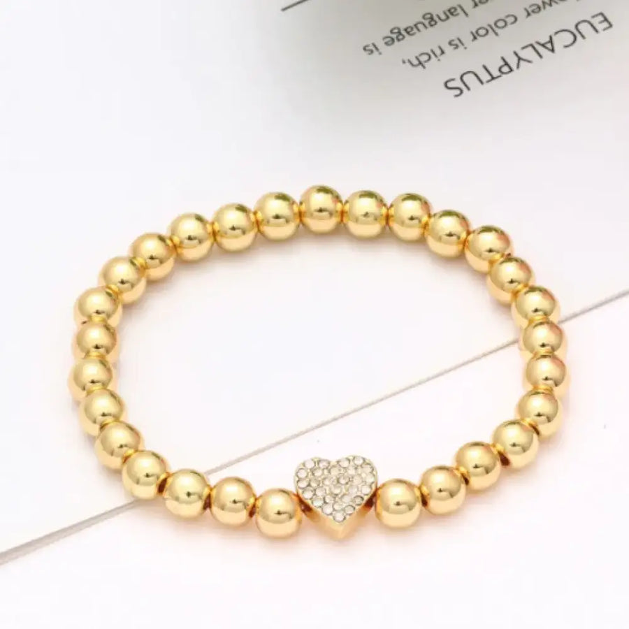 Gold-toned beaded bracelet featuring a central heart charm adorned with sparkling rhinestones.