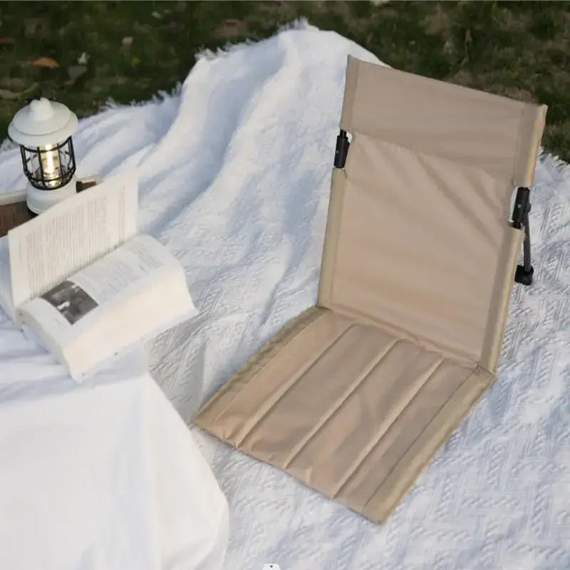 Beige foldable camping chair with padded seat and backrest, featuring black metal frame clips for easy setup.