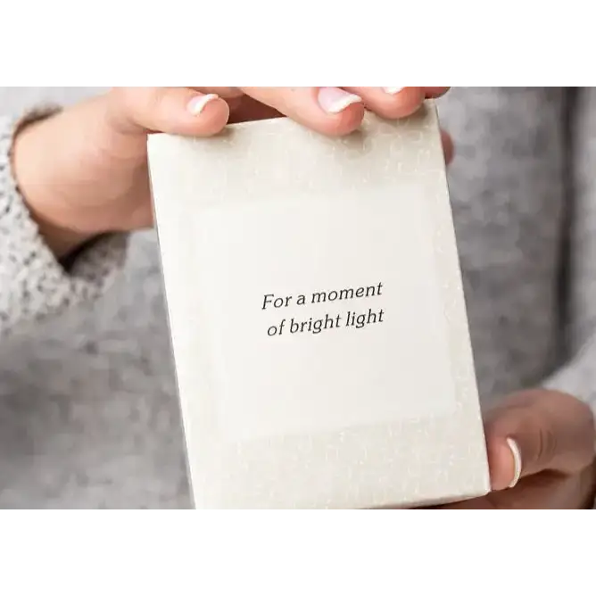 A cream-colored, textured card with elegant black text reading ’for a moment of bright light.’