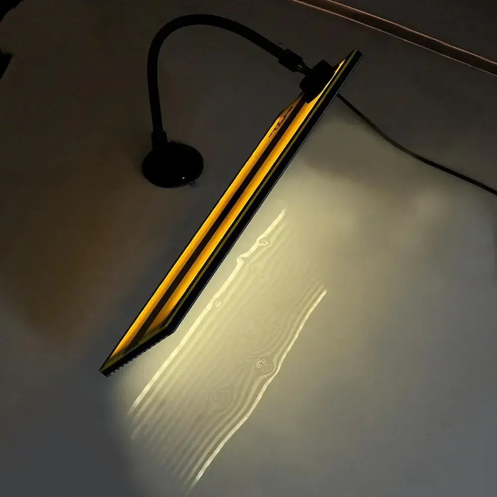 A sleek, black gooseneck desk lamp with a long, narrow rectangular light panel that emits warm yellow illumination.
