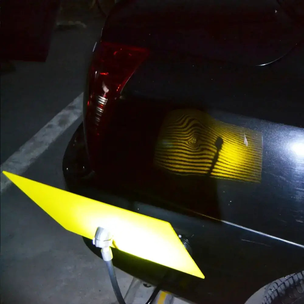 Yellow triangular parking aid attached to a black car’s rear bumper