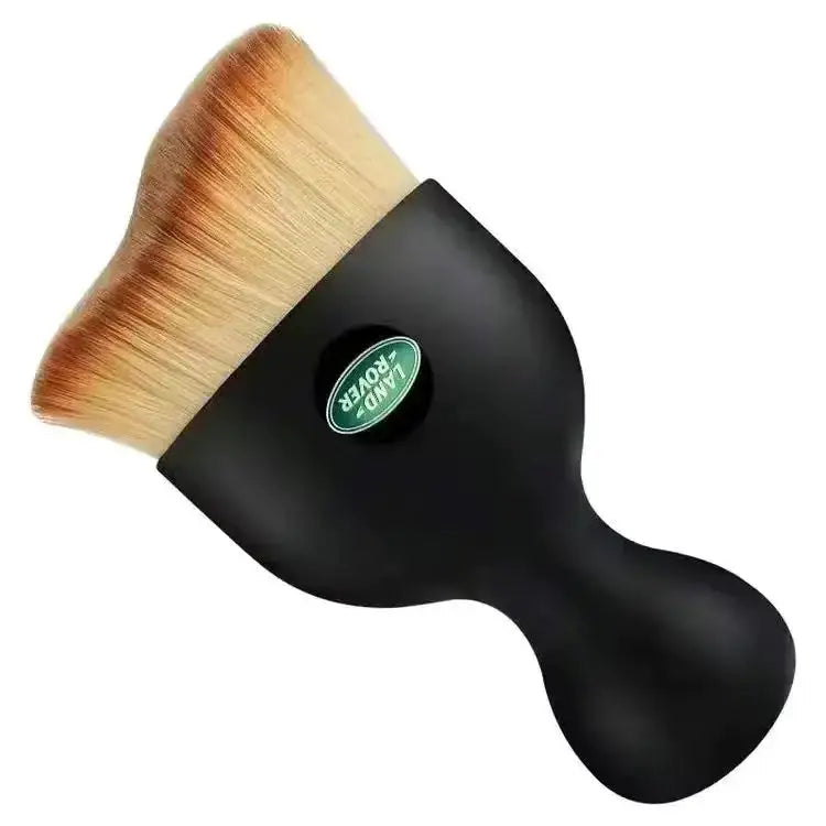 Black-handled makeup brush with a dense, tapered head of light brown and beige synthetic bristles featuring the green land rover logo on its handle.