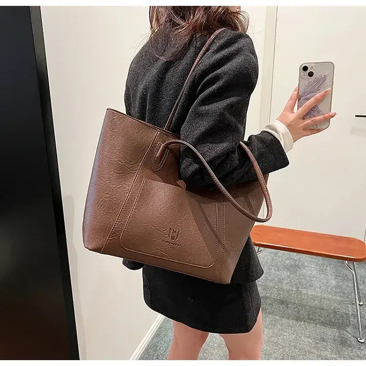Brown leather tote bag with a front pocket and embossed logo.