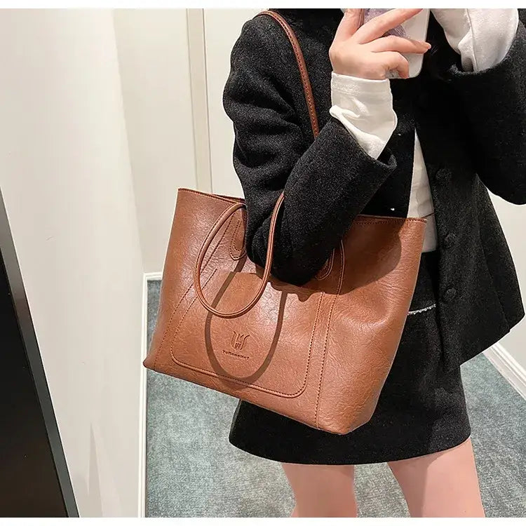 Brown leather tote bag with a subtle embossed logo on the front.