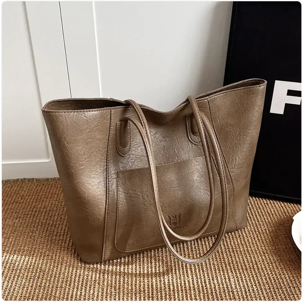 A taupe-colored, textured faux leather tote bag with matching handles and a subtle logo on the front.