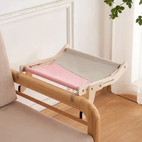 A minimalist wooden pet bed with a pink and gray fabric hammock.