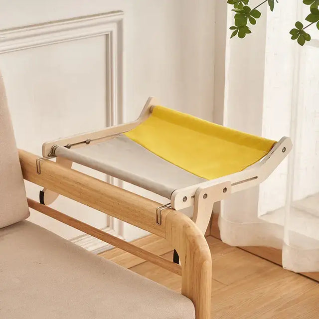 A minimalist wooden cat hammock with a two-tone fabric sling in yellow and gray, designed for comfort on furniture.