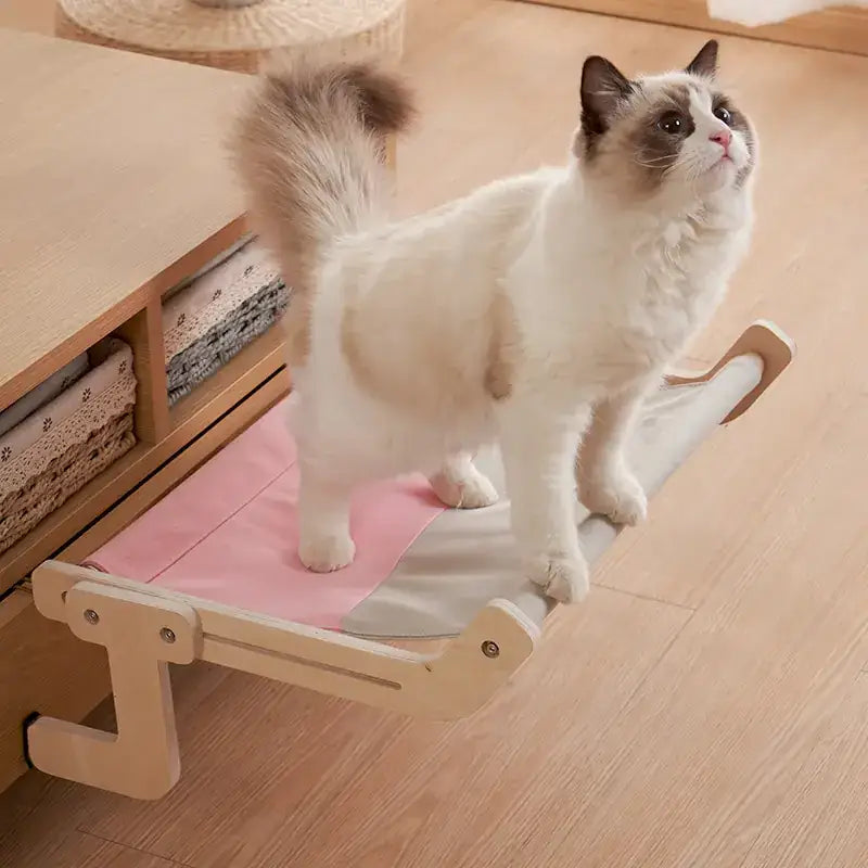 A soft pink and gray fabric cat bed with a light wood frame, designed for cozy resting.