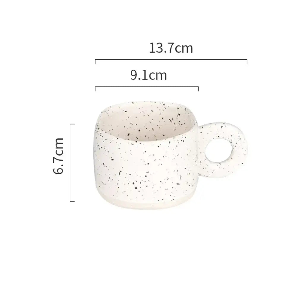 A white ceramic mug with black speckles and a circular handle.