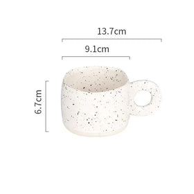 A white ceramic mug with black speckles and a circular handle.