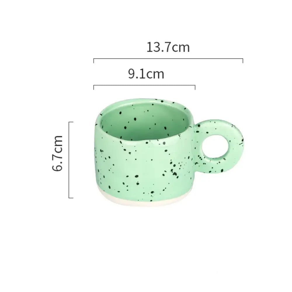 A mint green ceramic mug with black speckles and a white base, featuring a rounded handle.