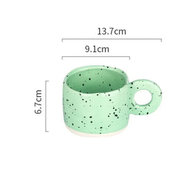 A mint green ceramic mug with black speckles and a white base, featuring a rounded handle.