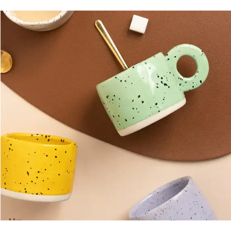 Mint green ceramic mug with black speckles and a white rim, featuring a circular handle.