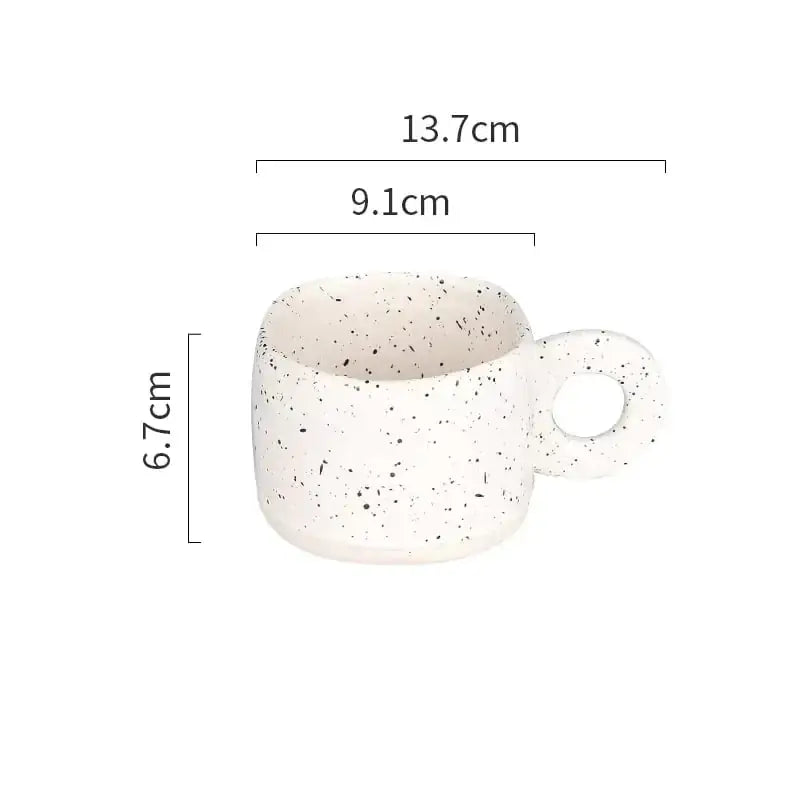 A white ceramic mug with black speckles and a circular handle.