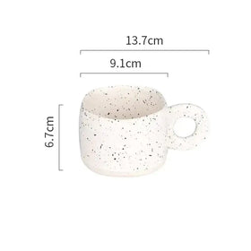 A white ceramic mug with black speckles and a circular handle.