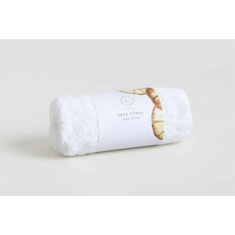 A plush white cotton face towel, neatly rolled and wrapped with a minimalist label featuring gold-toned leaf accents.