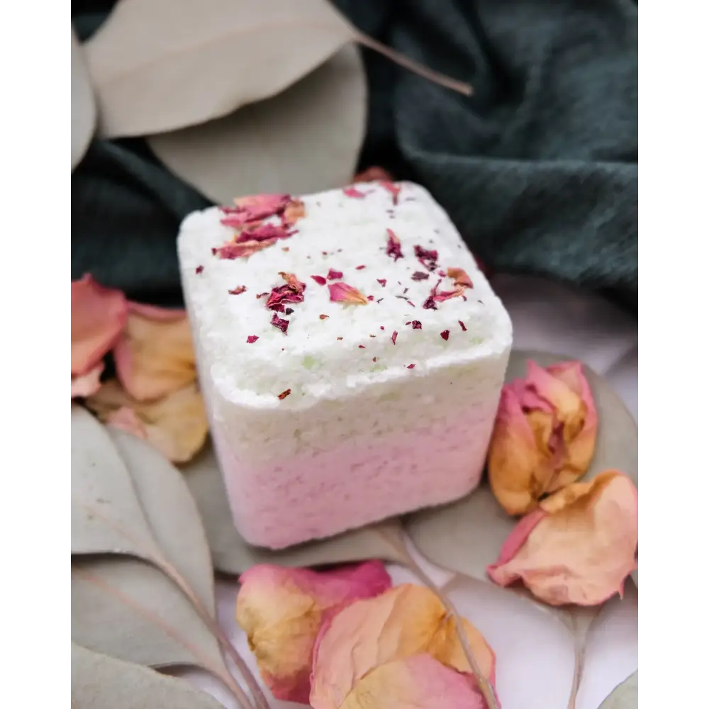A square-shaped bath bomb with a gradient from white to pink, topped with dried rose petals.