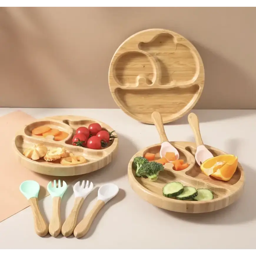 Light brown bamboo children’s meal plates with segmented compartments and matching wooden spoons, forks, and a spoon in pastel mint green and white.