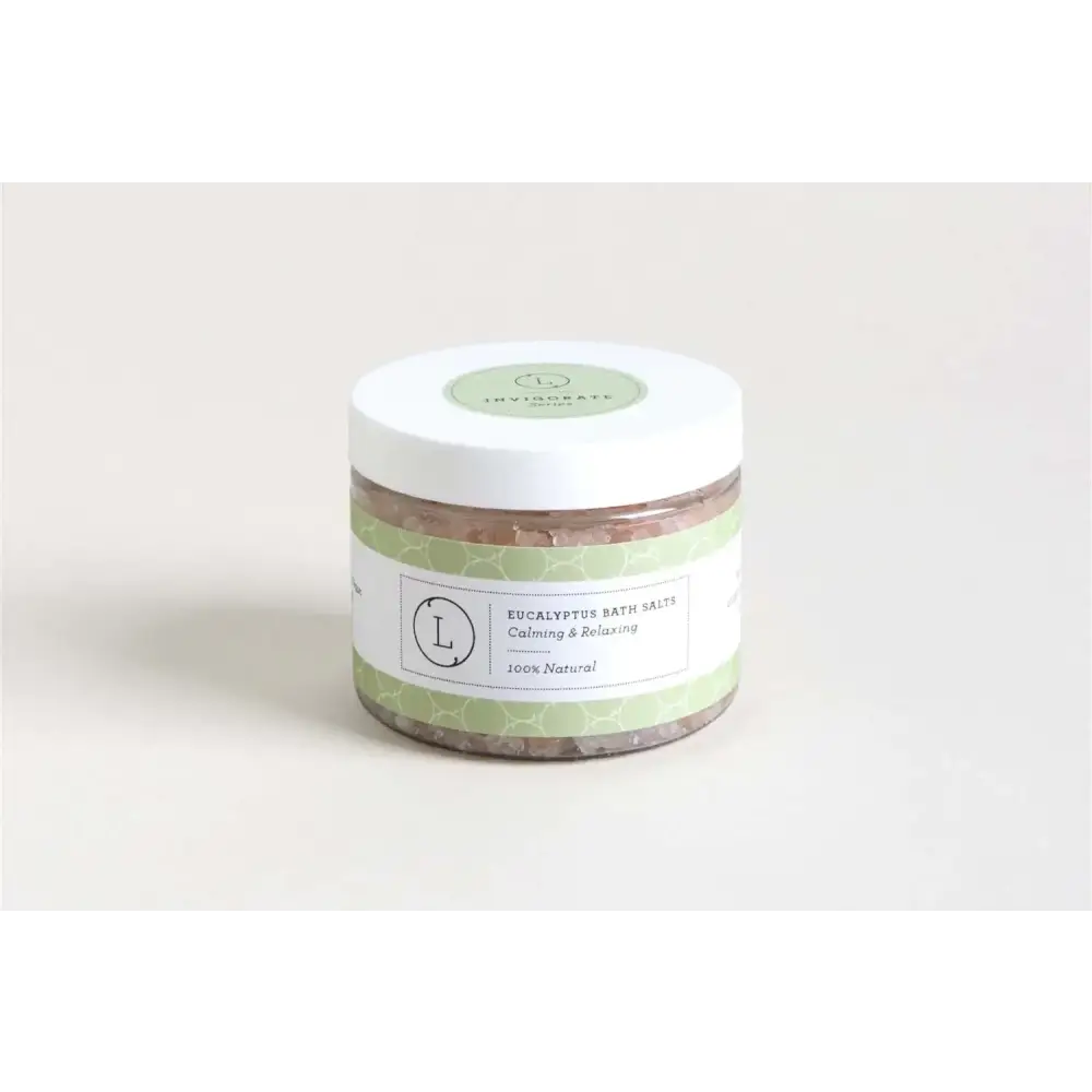 A clear glass jar with a white lid and light green patterned label, containing eucalyptus bath salts.