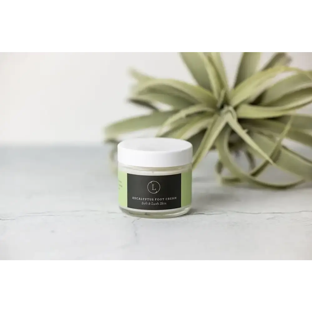 A clear glass jar with a white lid and a black label, containing eucalyptus foot cream.