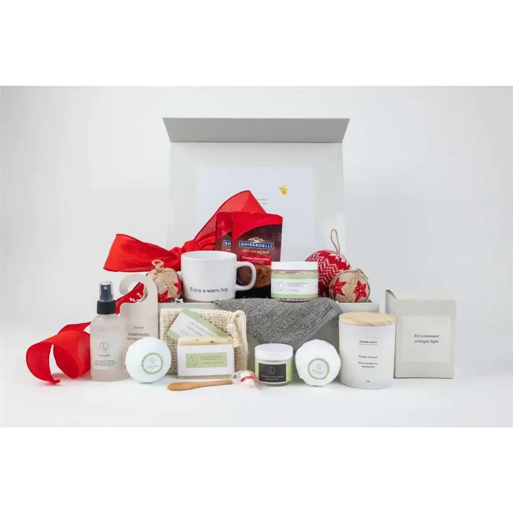 White ceramic mug with ’enjoy a warm hug’ printed in black script, nestled among festive holiday gift items