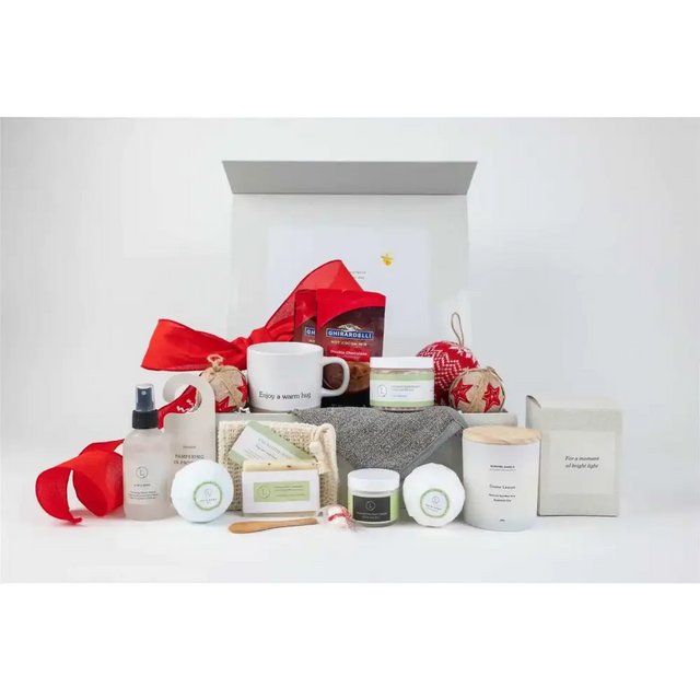 White ceramic mug with ’enjoy a warm hug’ printed in black script, nestled among festive holiday gift items