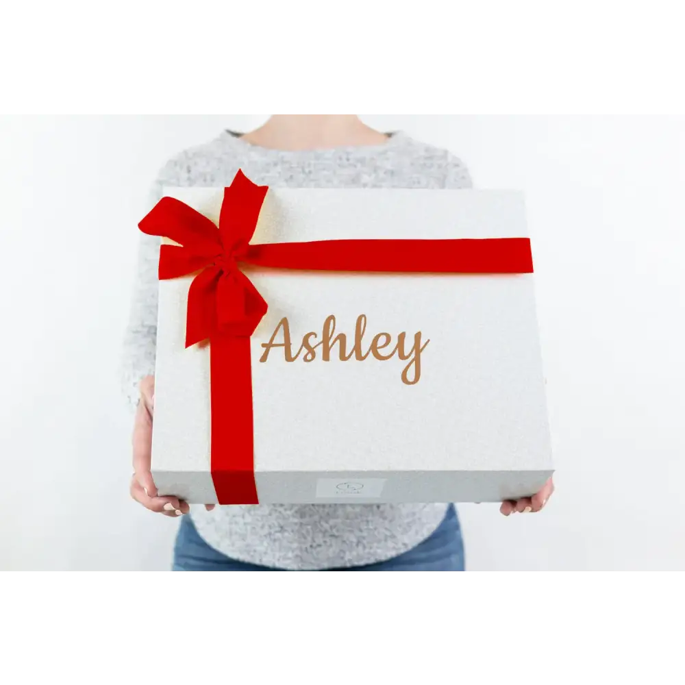 White gift box with a red ribbon bow and the name ’ashley’ in gold cursive lettering.