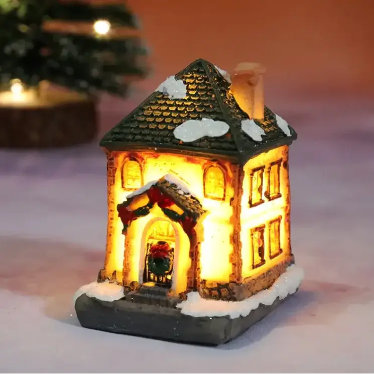 A warmly lit miniature christmas house figurine with a green tiled roof, snow-dusted details, and festive wreath decorations.
