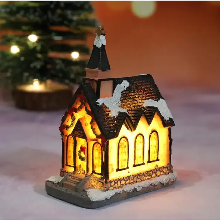 A warmly lit miniature christmas church figurine with a black shingled roof, snow-dusted details, and arched windows glowing from within.